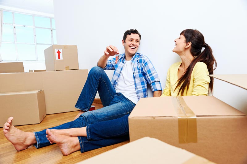 Couple sitting among moving boxes holding the keys to their new home